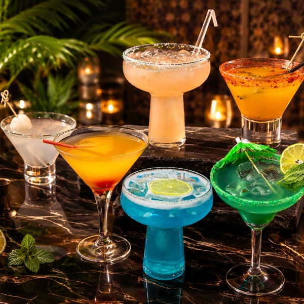 Vibrant cocktails on a dark marble bar with tropical plants and flickering candles.