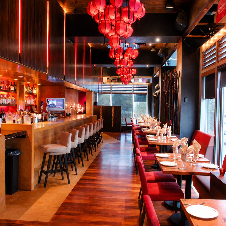 Asian-inspired restaurant interior with a long bar, red chairs, and decorative red lantern lighting.