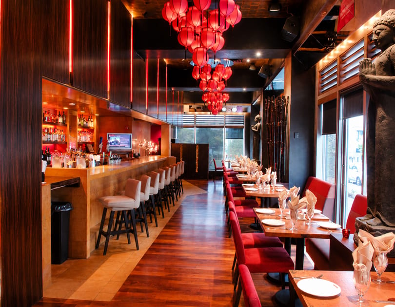 Asian-inspired restaurant interior with a long bar, red chairs, and decorative red lantern lighting.