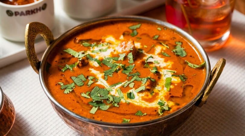 A copper bowl of butter chicken curry, garnished with cream swirls and fresh cilantro.