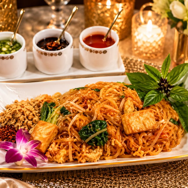 Delicious Pad Thai with tofu, peanuts, and a purple orchid, presented on a festive table with sauces.
