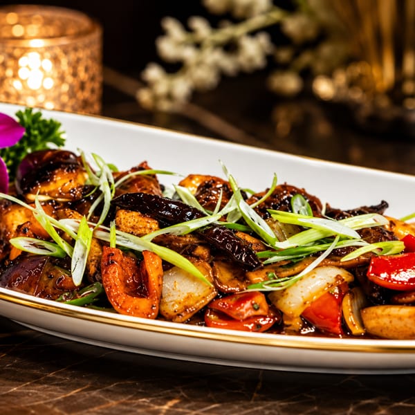 Stir-fried vegetables in a rich dark sauce, garnished with green onions and a purple orchid.