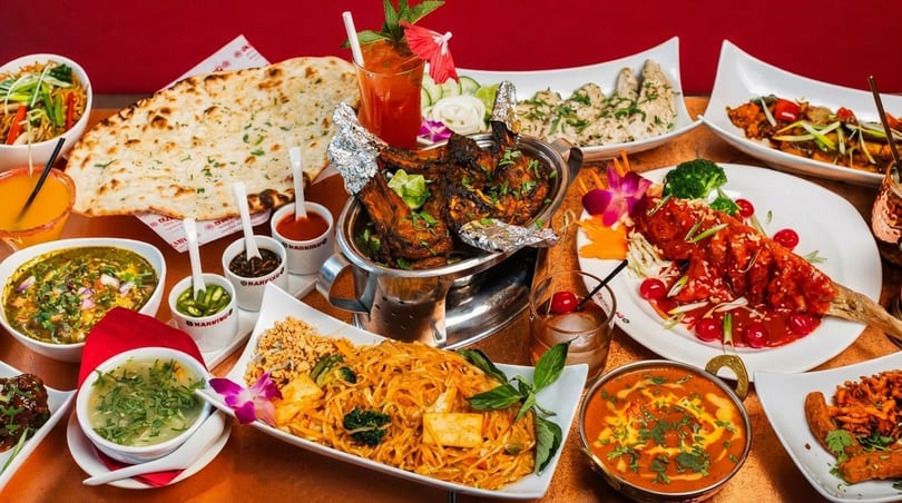 A vibrant spread of Indian and Asian dishes, including naan, curries, noodles, and grilled meats.