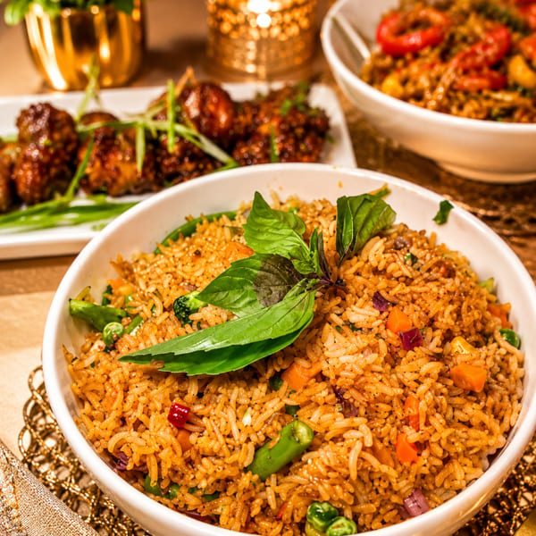 Vegetable fried rice with basil, chicken wings, and another rice dish on a candlelit restaurant table.