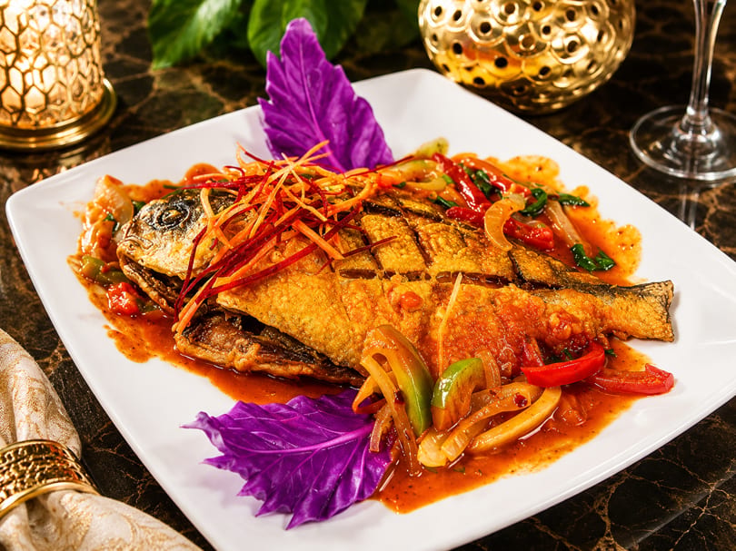 Golden fried whole fish with vibrant red sauce, bell peppers, onions, and shredded garnish.