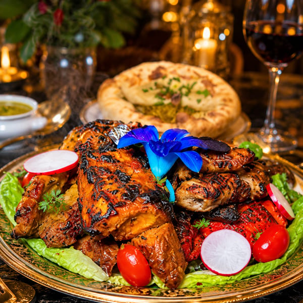 Grilled chicken and meats on a golden platter with garnishes, naan, and wine on an elegant restaurant table.