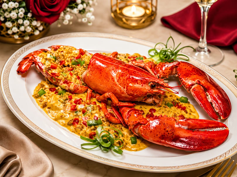 Whole cooked lobster in a creamy sauce with peppers and green onions on an elegant dining table.